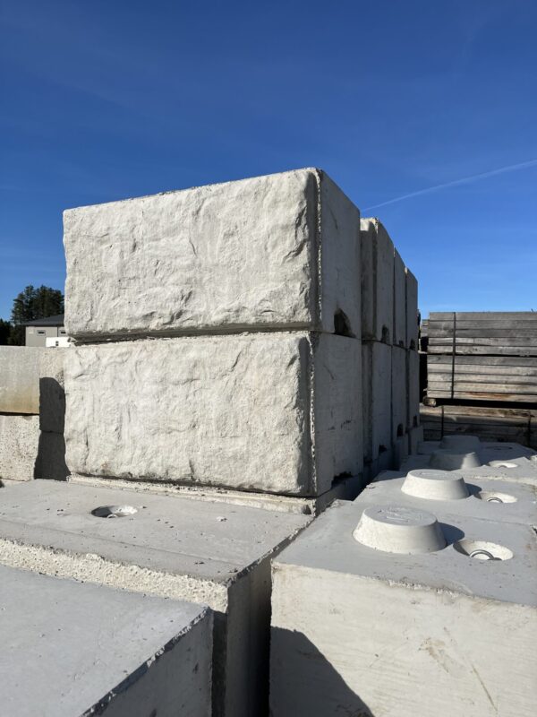 Large concrete blocks stacked outdoors under a clear blue sky, with a few trees visible in the background. No people or landmarks present.