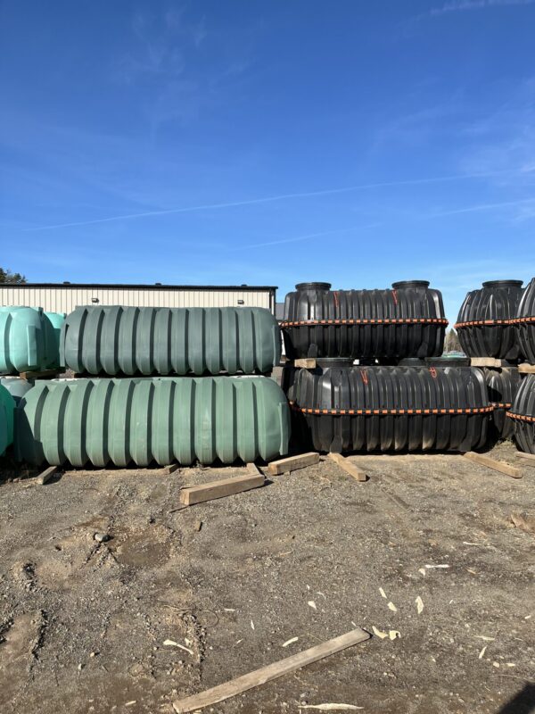 Large, industrial water tanks are stacked outdoors on a dirt lot under a clear blue sky, with a warehouse building in the background.