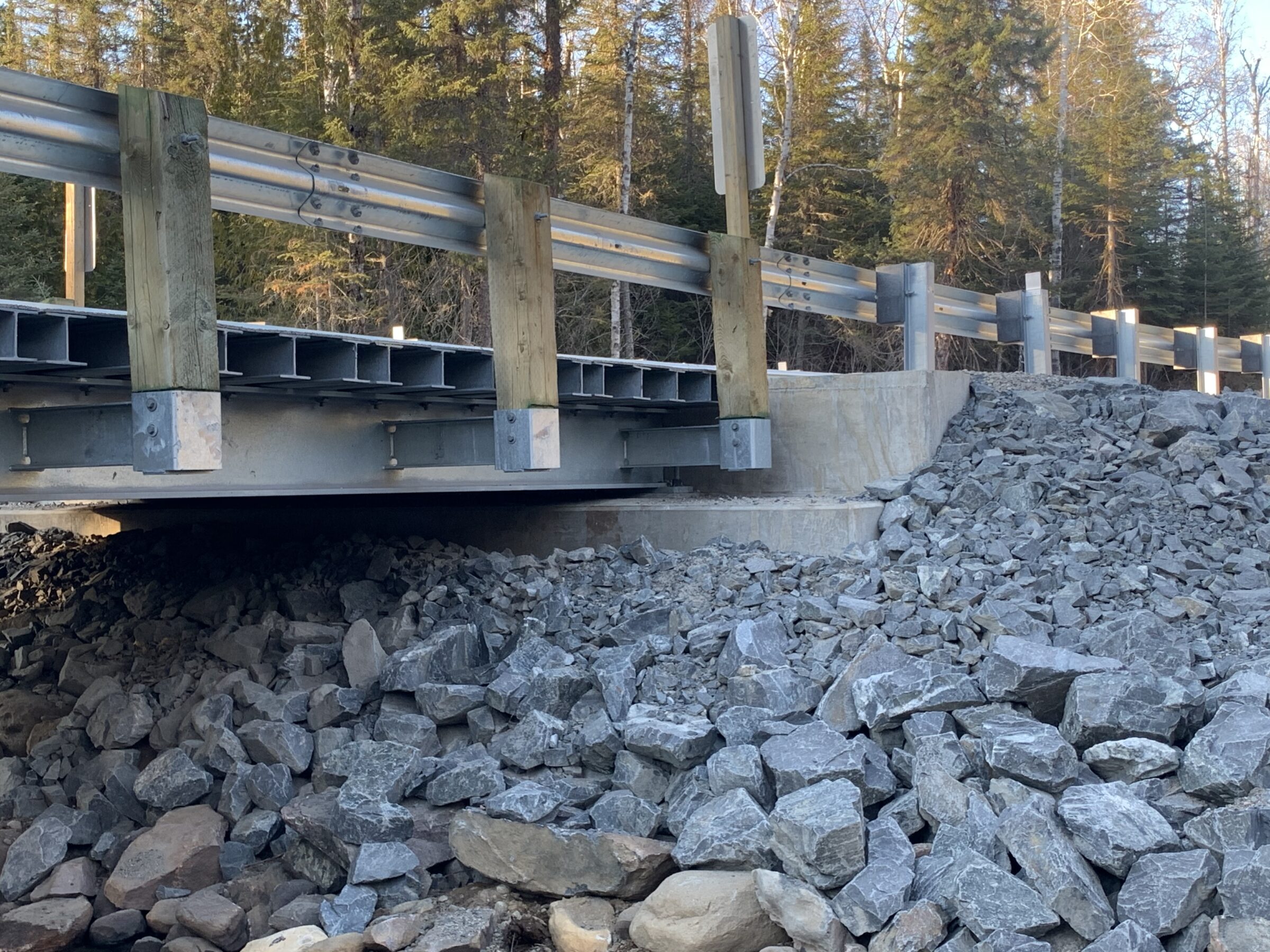 A small bridge over a rocky embankment with guardrails; surrounded by dense forest and no visible landmarks or people present.