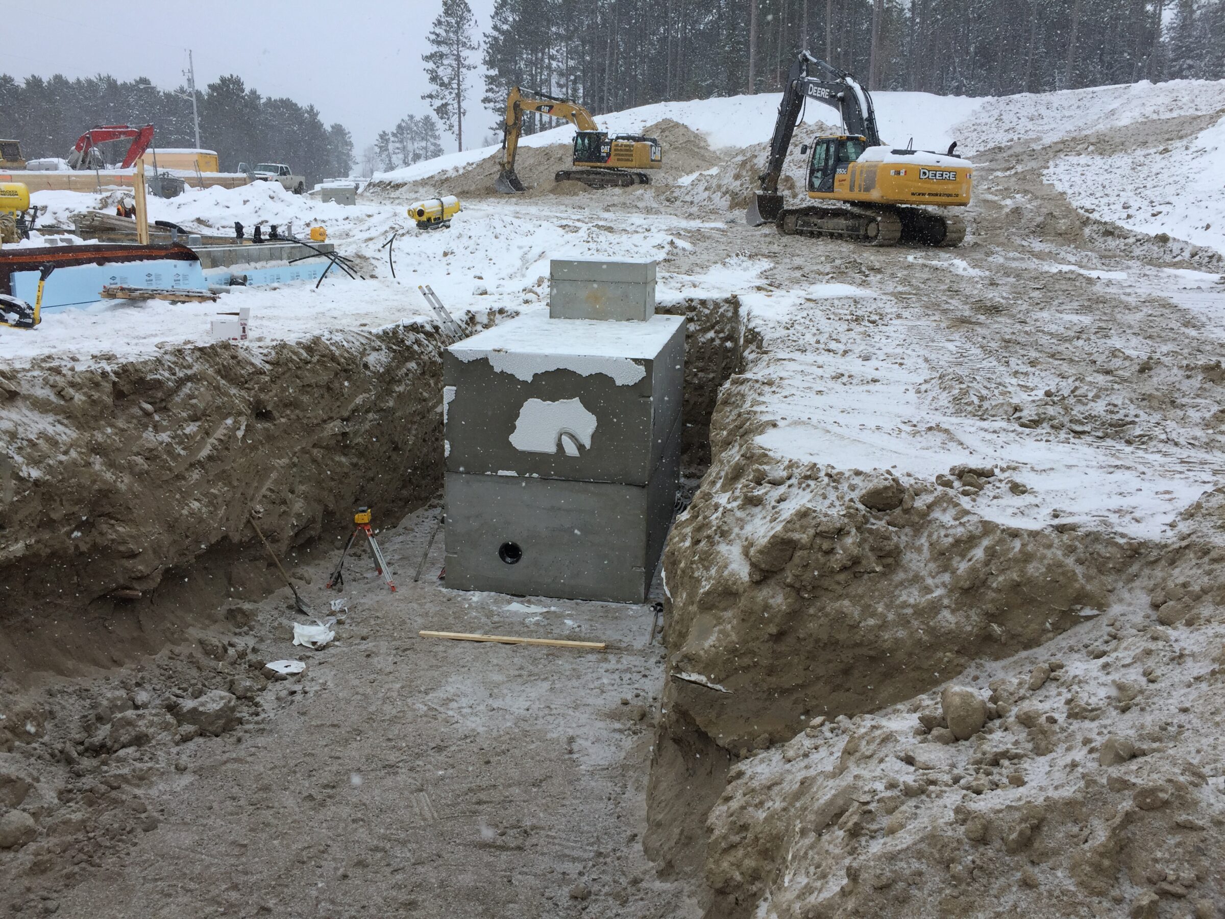 Construction site with heavy machinery working in snowy conditions. Excavator and equipment visible, no recognizable landmarks or buildings present.