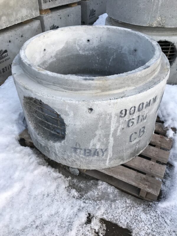 Concrete cylindrical structures stacked on a snowy ground, with visible industrial markings, resting on wooden pallets. Heavy-duty construction site elements.