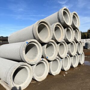 A stack of large concrete pipes arranged in a pyramid on a construction site, with a shadow of a person visible.