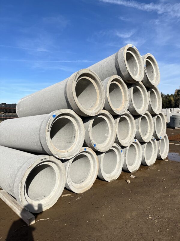 A stack of large concrete pipes arranged in a pyramid on a construction site, with a shadow of a person visible.