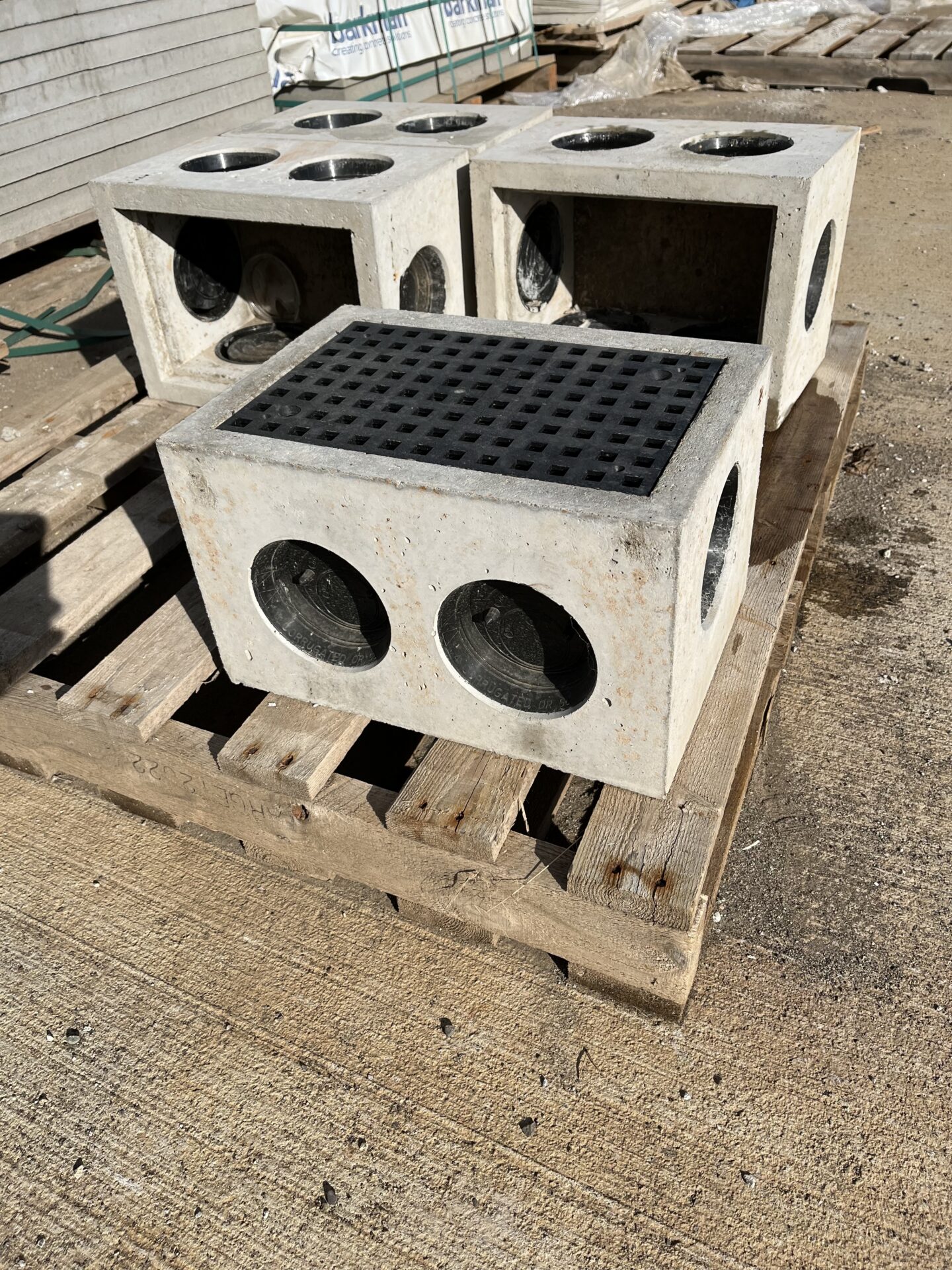 Concrete blocks with circular holes are stacked on wooden pallets at a construction site. There are no people or recognizable landmarks present.